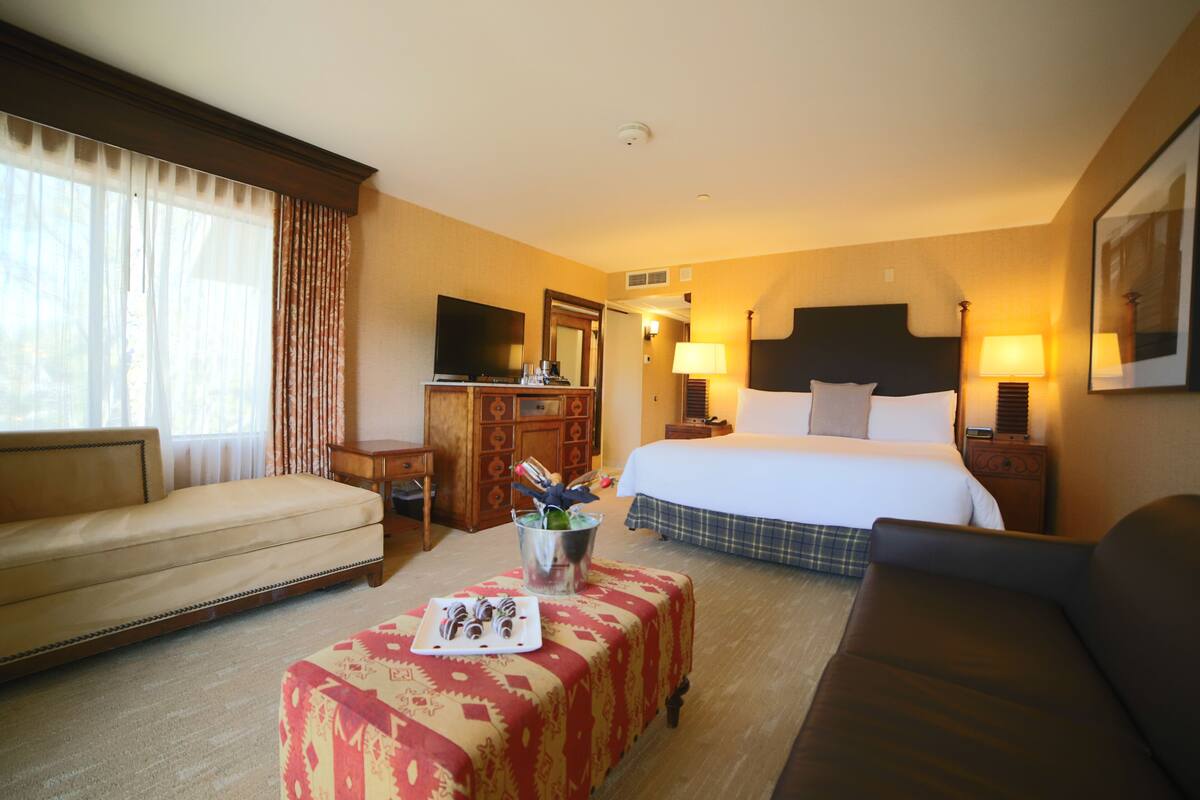Habitación de hotel con cama, sofá, escritorio, televisor y mesa con bandeja de pasteles.