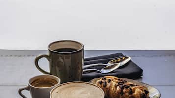 A table with a coffee cup, a mug, and a pastry on a balcony overlooking a snowy landscape.