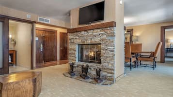A modern living room with a stone fireplace, a flat-screen TV mounted above it, and a dining area with a wooden table and chairs.