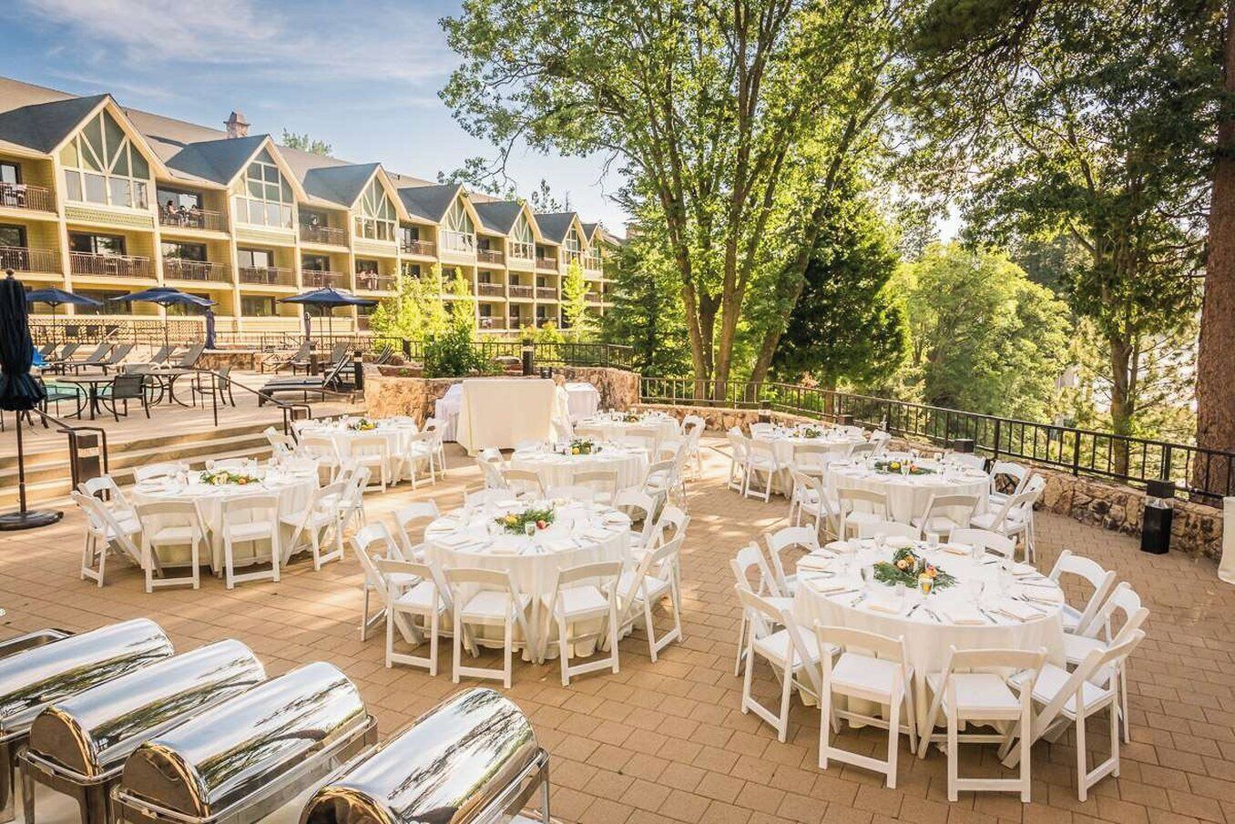 An outdoor patio with round tables and chairs, a stone wall, and a building with multiple balconies in the background.