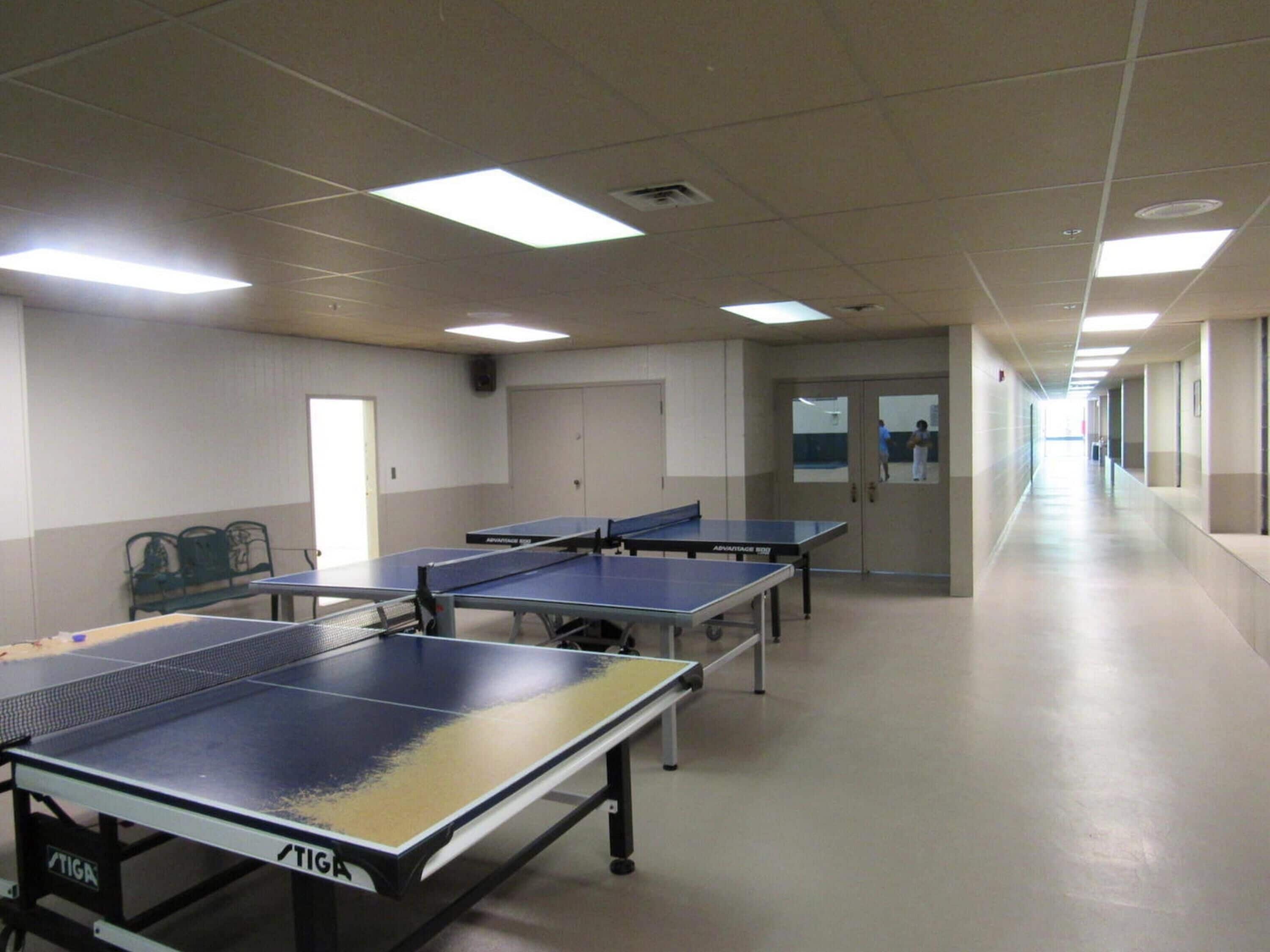 A corridor with multiple ping pong tables, a bench, and doors along the walls.