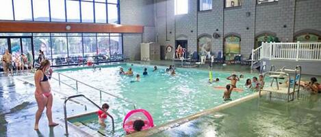 An indoor swimming pool with multiple lanes, a diving board, and a spectator area.