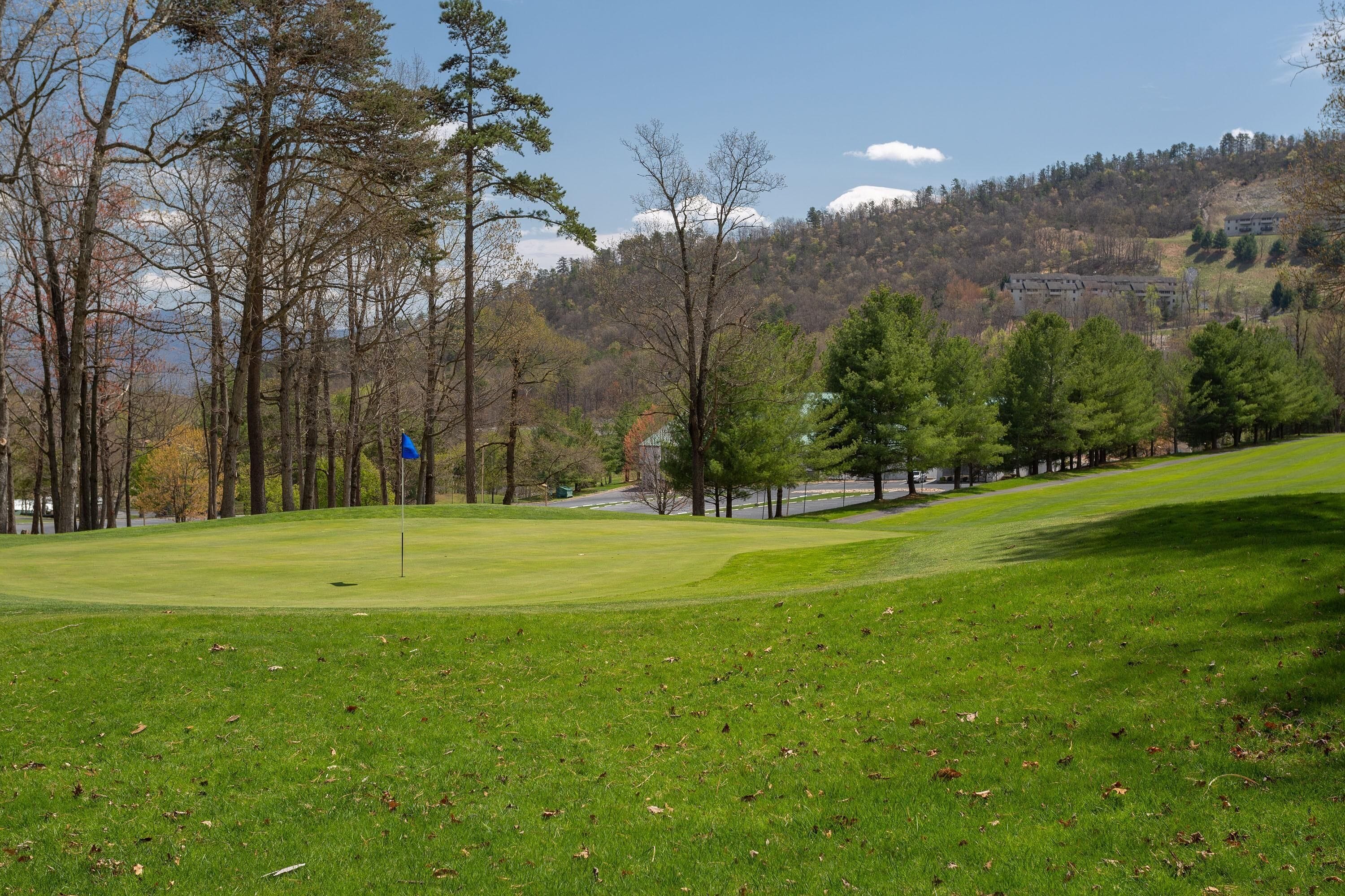 A golf course with a clear sky, trees, and a distant building.