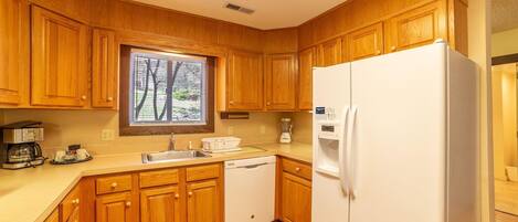 Una cocina compacta con armarios de madera, un refrigerador blanco, un lavavajillas y una ventana con persianas.