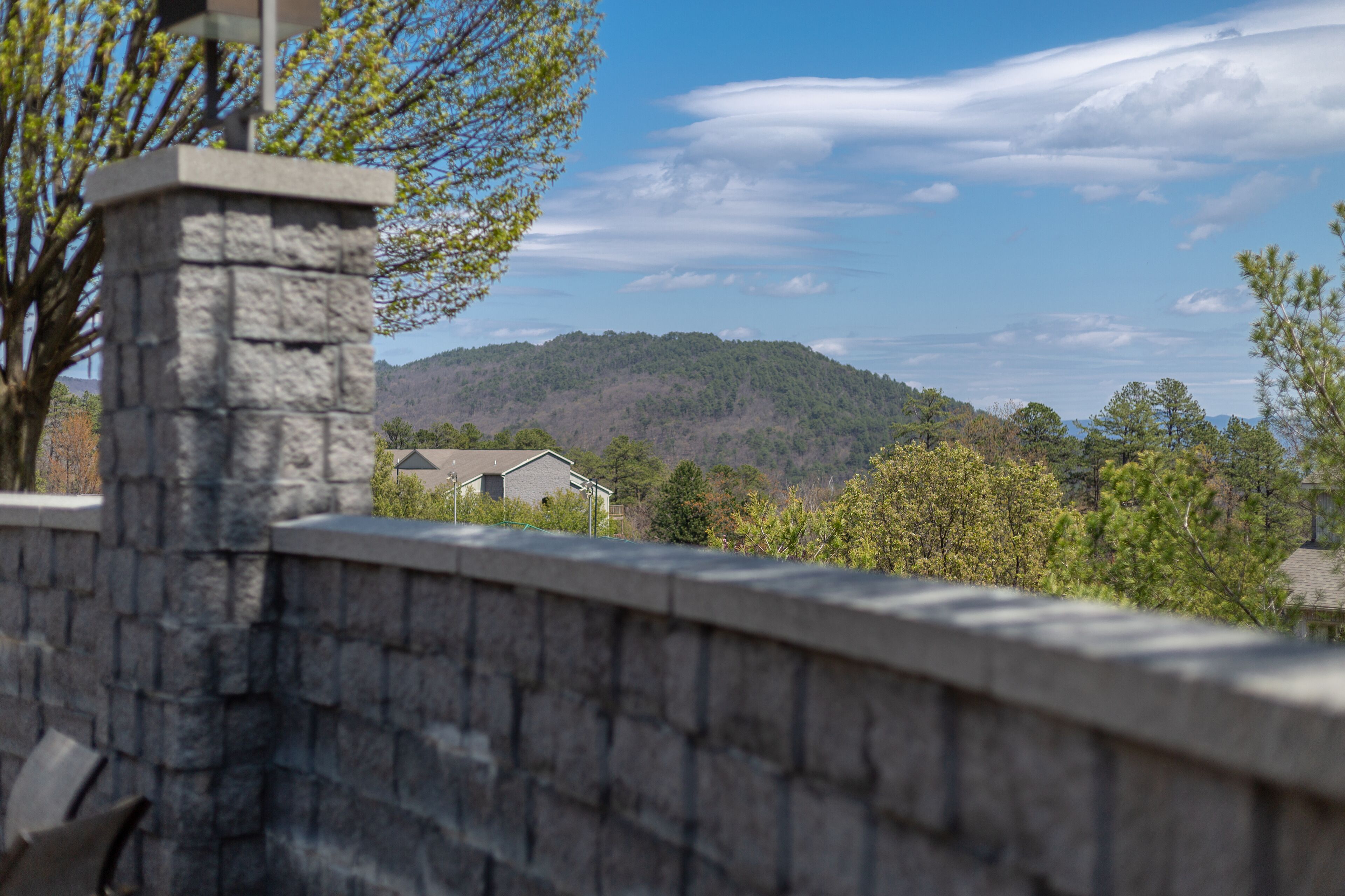 A stone wall with a view of a house and a forested hill in the background.