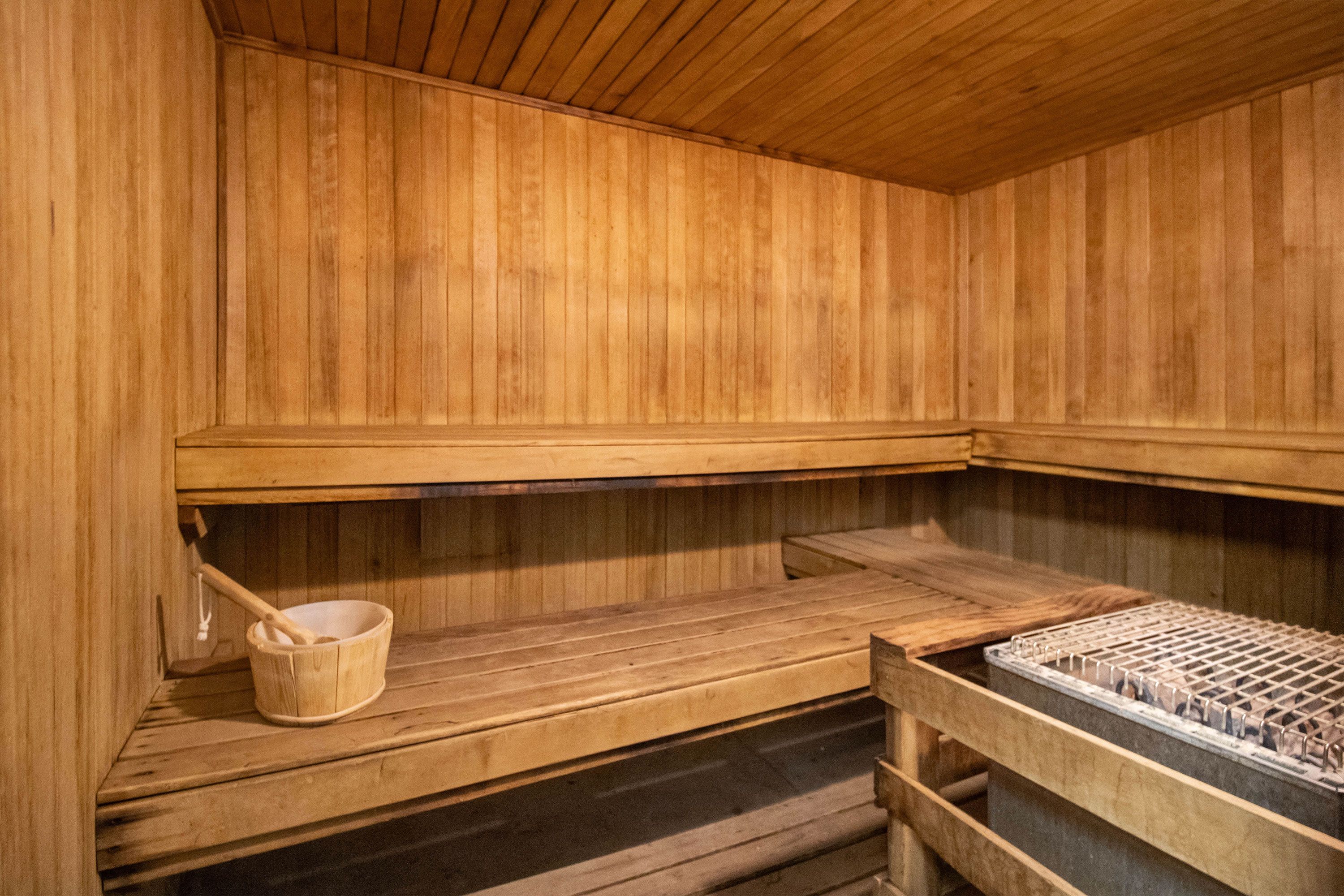 Un sauna avec des bancs en bois, un seau en bois et une étagère en métal.