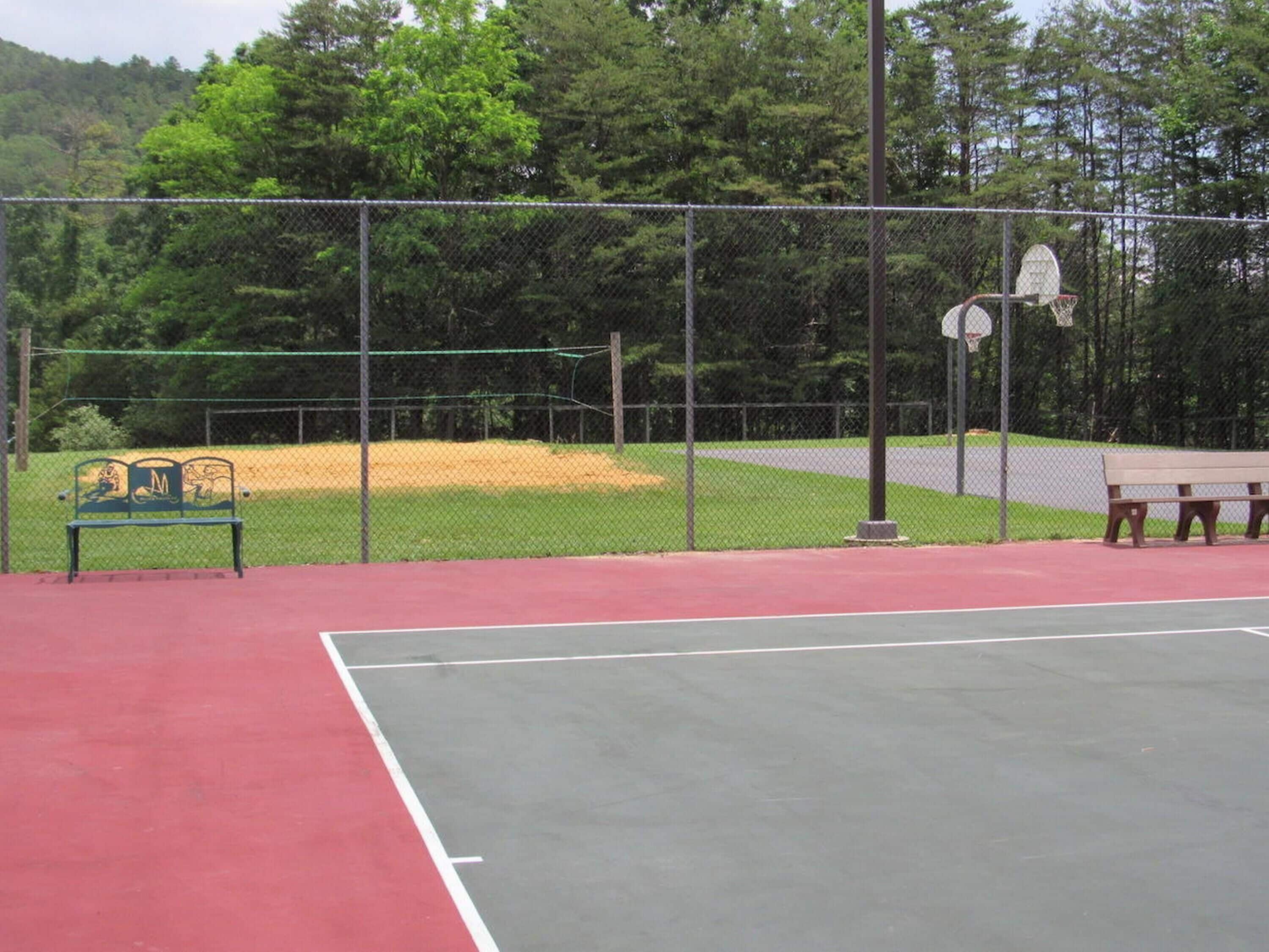 Un terrain de tennis entouré d’une clôture, avec un banc et un panier de basket.