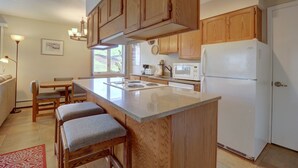Una cocina con armarios de madera, un refrigerador blanco, un microondas y un comedor con mesa y sillas.