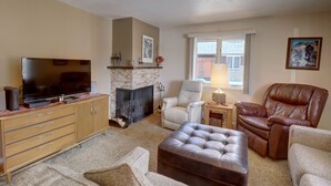 Una sala de estar con chimenea, televisor y asientos cómodos, incluyendo un sillón de cuero y un sofá.