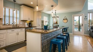 A kitchen with white cabinets, a granite countertop, a bar area with stools, and pendant lighting.
