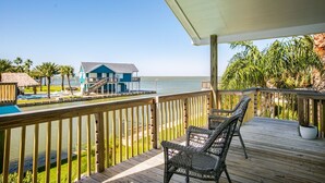 A wooden deck with wicker chairs, a pool, and a view of a blue building across the water.