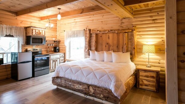 A log cabin interior with a wooden bed, a kitchenette, and a dining area. - Cozy Lodge Fireplace Suite in Ohio's Amish Country (Millersburg)