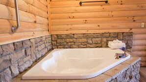 A wooden cabin interior with a stone wall, a wooden ceiling, and a white bathtub with a stone countertop. - Cozy Lodge Fireplace Suite in Ohio's Amish Country (Millersburg)