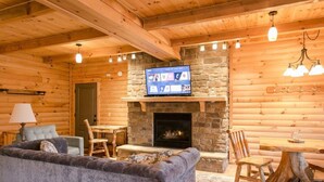 A cozy log cabin interior with a stone fireplace, wooden furniture, and a television mounted above it. - Cozy Lodge Fireplace Suite in Ohio's Amish Country (Millersburg)