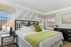 A bedroom with a bed, bedside table, lamp, and a window with curtains.