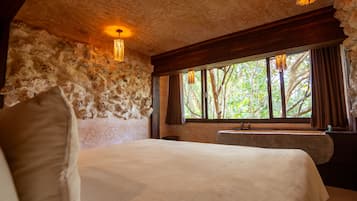 A bedroom with a stone wall, a bed, a window with curtains, and a hanging light fixture.