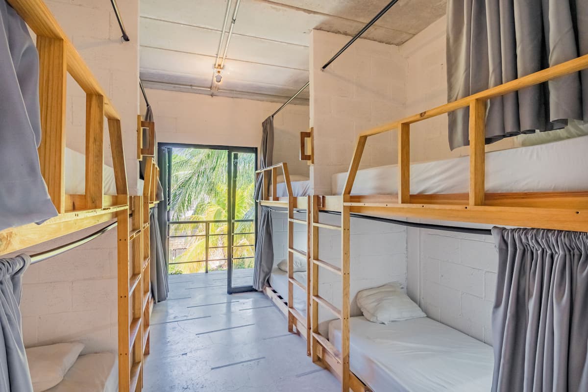 A corridor with bunk beds, wooden railings, and a view of greenery outside.