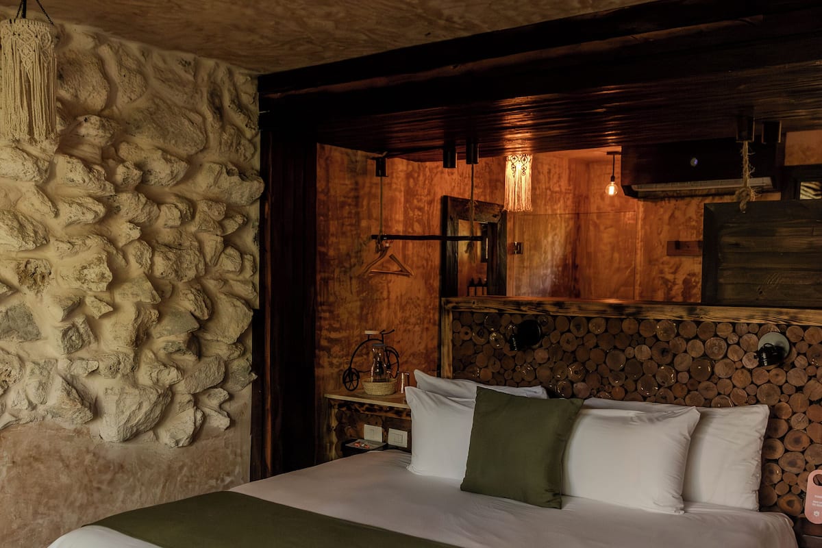 A bedroom with a stone wall, a wooden headboard, and a bed with white bedding and a green throw.