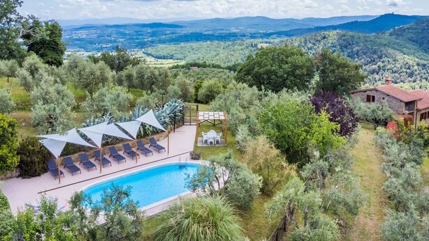 Ein Poolbereich mit Liegestühlen und Sonnenschirmen, umgeben von üppiger Vegetation und Blick auf ferne Hügel.