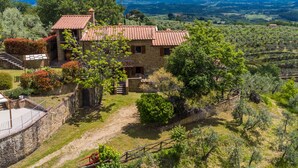 Ein Haus aus Stein mit rotem Ziegeldach, umgeben von üppiger Vegetation und Blick auf ferne Berge.