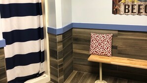 Una habitación con cortina de ducha a rayas, un banco con cojín estampado y un cartel de colores en la pared.