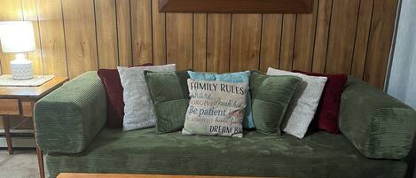 A green sofa with multiple cushions and a wooden coffee table in front.