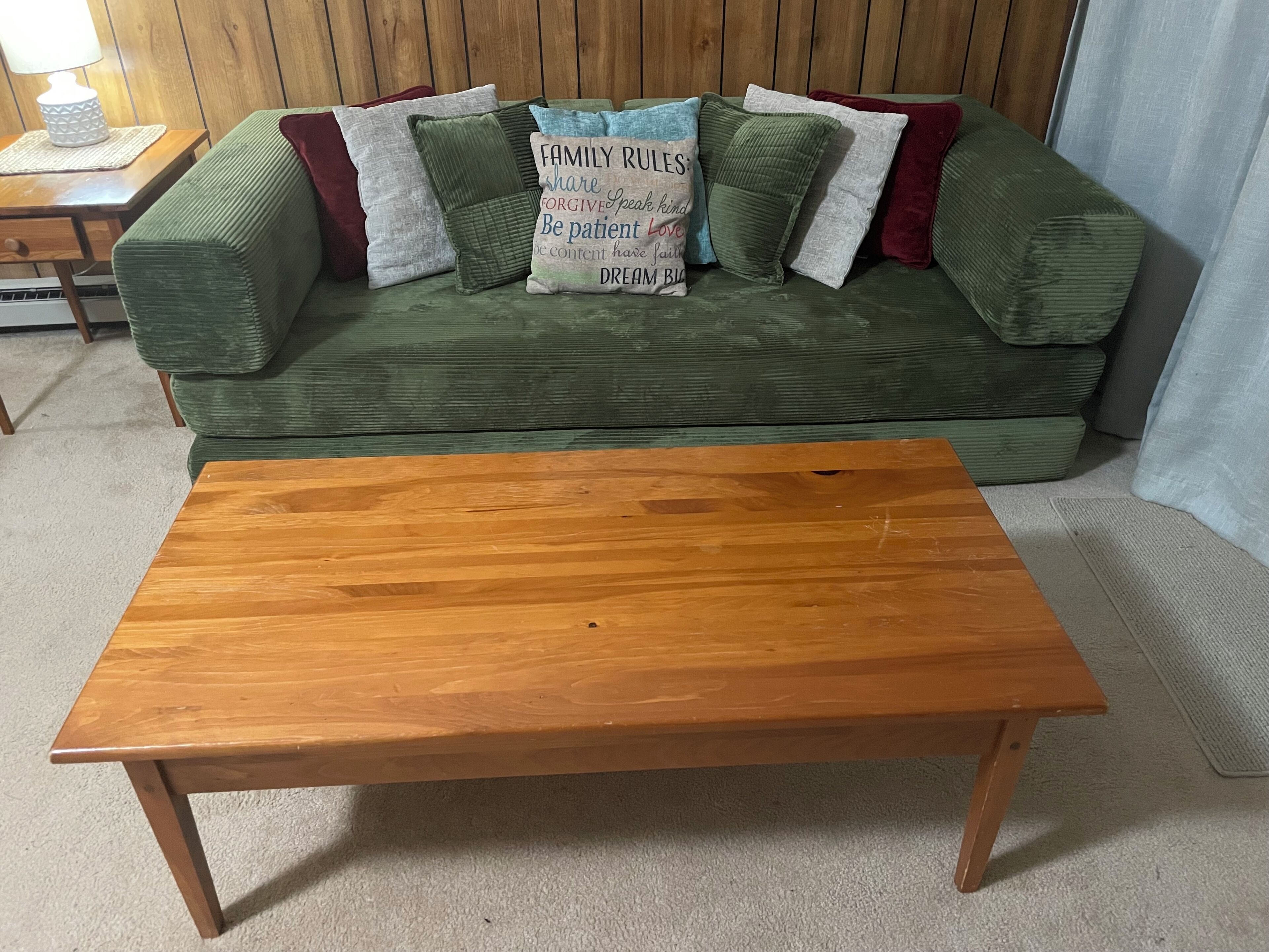 Ein grünes Sofa mit vielen Kissen, ein Couchtisch aus Holz und eine Lampe auf einem Holztisch.