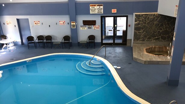 Una piscina interior con una marca de profundidad de 3 pies, rodeada de sillas y varios carteles en las paredes.