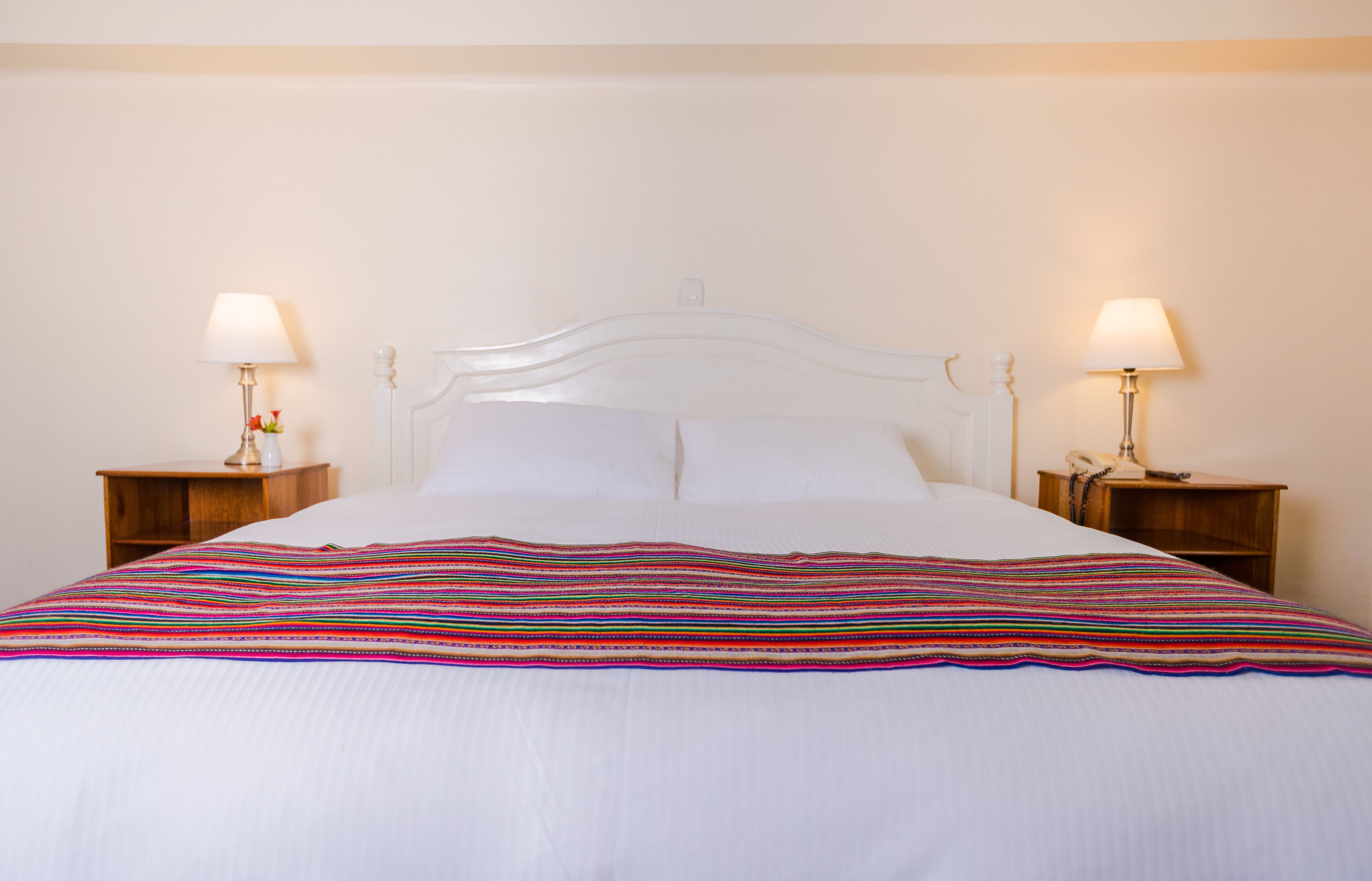 A neatly made bed with a colorful striped blanket, two bedside tables with lamps, and a simple white headboard.