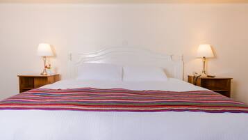 A neatly made bed with a colorful striped blanket, two bedside tables with lamps, and a simple white headboard.