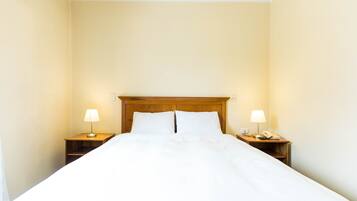 Una cama bien hecha con sábanas blancas, dos mesitas de noche con lámparas y un cabecero de madera.