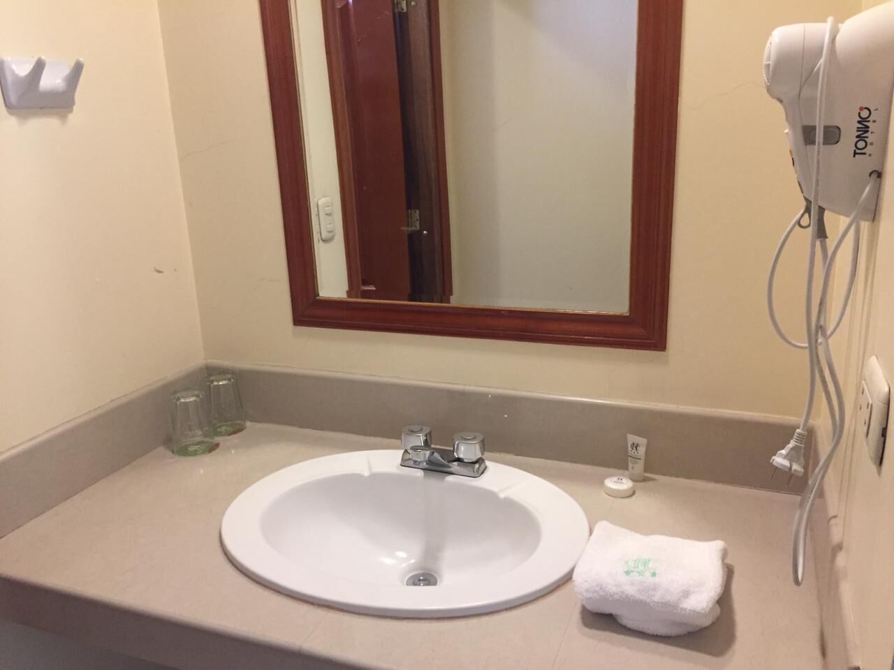 A bathroom with a white sink, a mirror with a wooden frame, a hairdryer, and a towel on the counter.