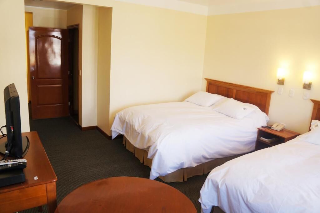 A hotel room with two beds, a desk with a television, and a door leading to another room.