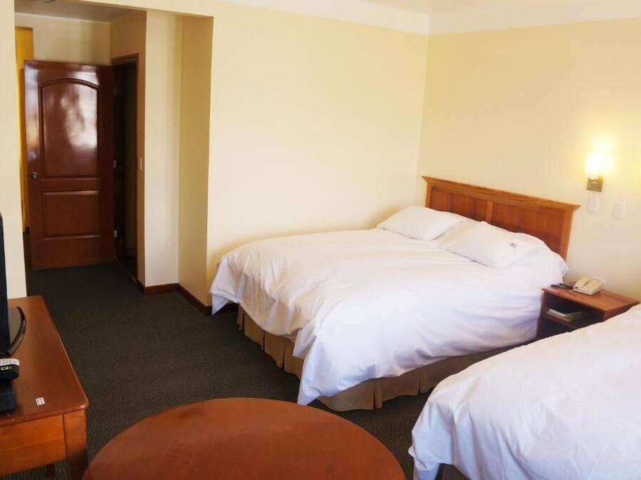 A hotel room with two beds, a desk with a television, and a door leading to another room.