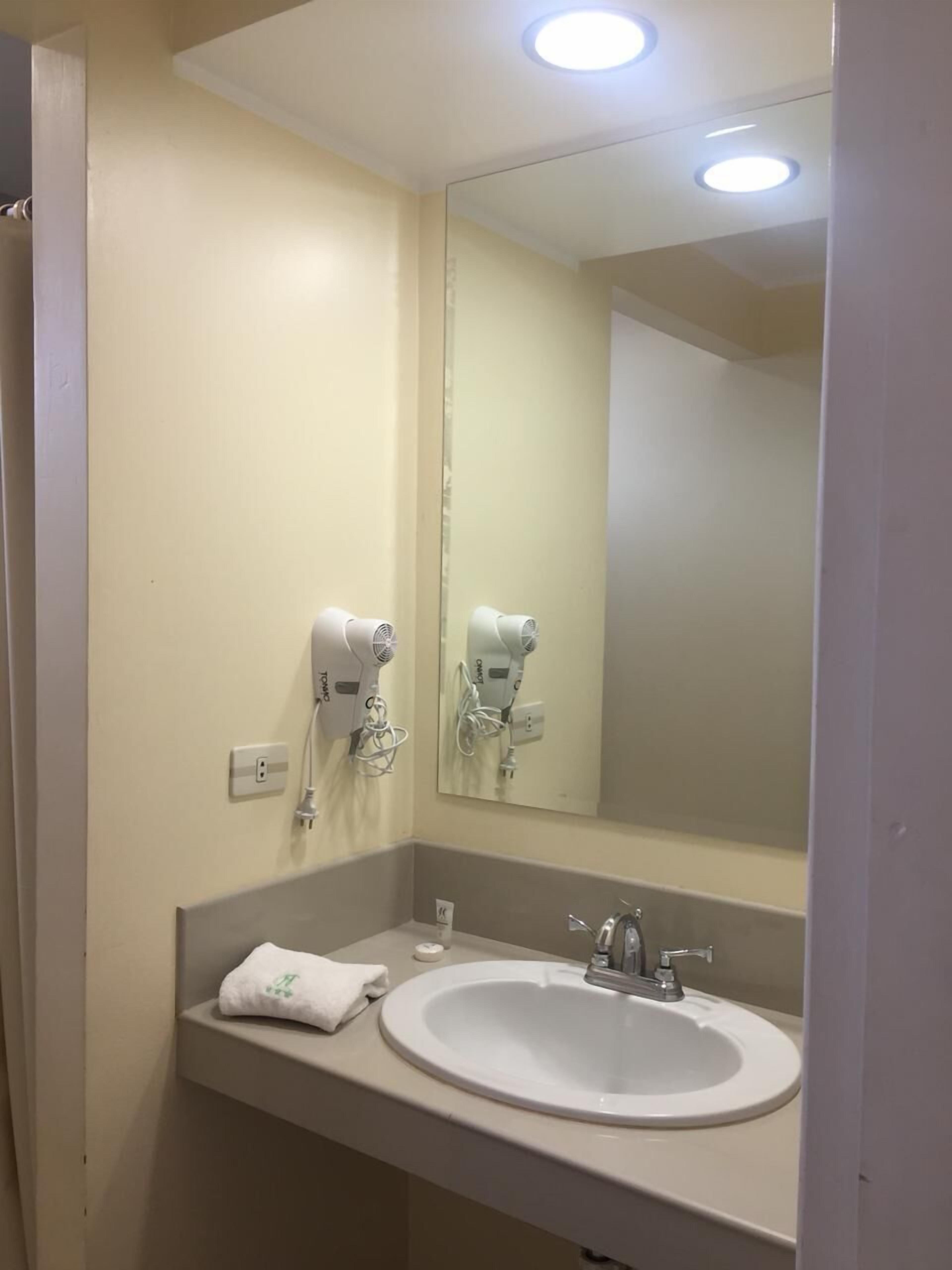 Een badkamer met een witte wastafel, een spiegel en twee haardrogers bevestigd aan de muur.