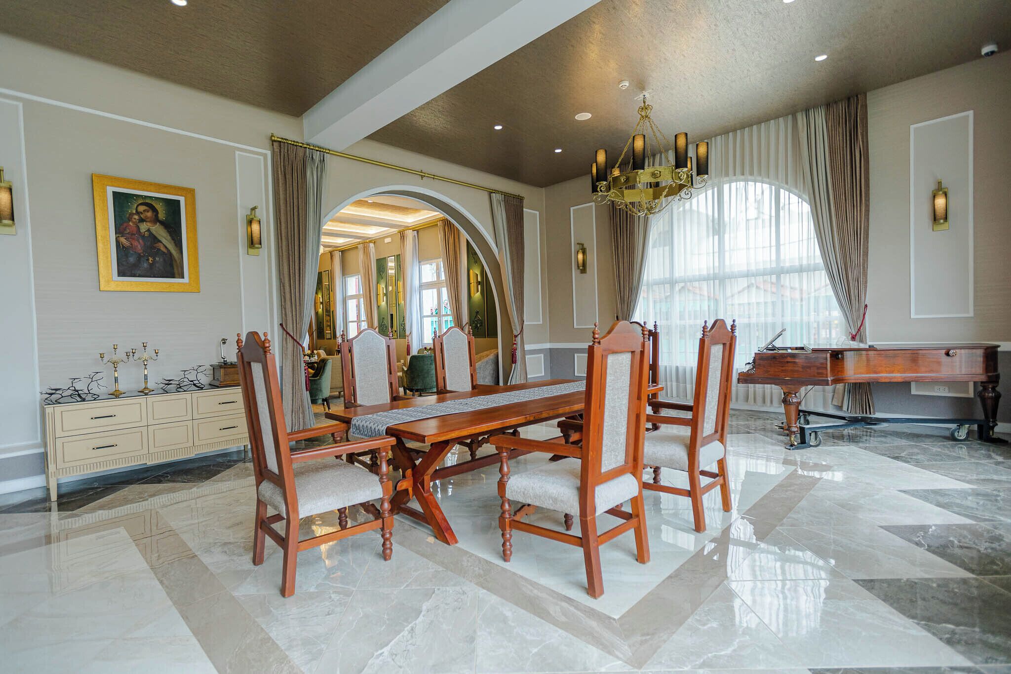 A spacious dining area with a large wooden table and chairs, a piano, and a mirror reflecting the room.