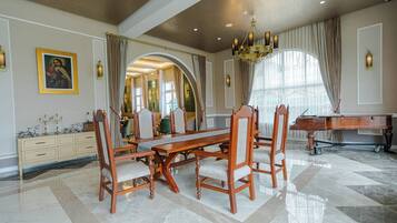 A spacious dining area with a large wooden table and chairs, a piano, and a mirror reflecting the room.