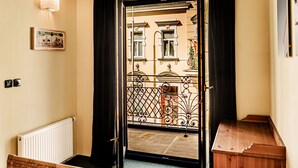 Ein Zimmer mit einer Holzbank, einem Heizkörper, einem schwarzen Vorhang und Blick auf einen Balkon mit Metallgeländer.