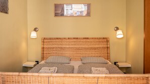 Ein Zimmer mit einem Rattan-Kopfteil, zwei Nachttischen, einem gerahmten Bild an der Wand und zwei Wandleuchten.