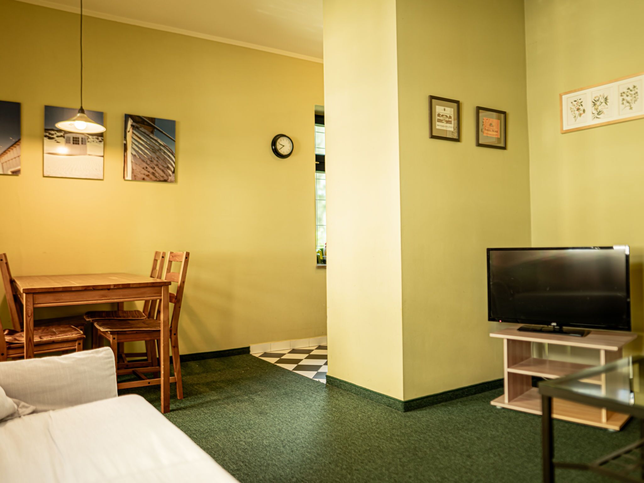 A hotel room with a bed, a wooden dining table with chairs, a television on a stand, and artwork on the walls.