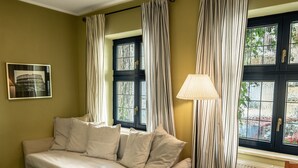 A room with a beige sofa, striped curtains, a lamp, and a window with a view of greenery. - Kipling by Interhome (Marianske Lazne)