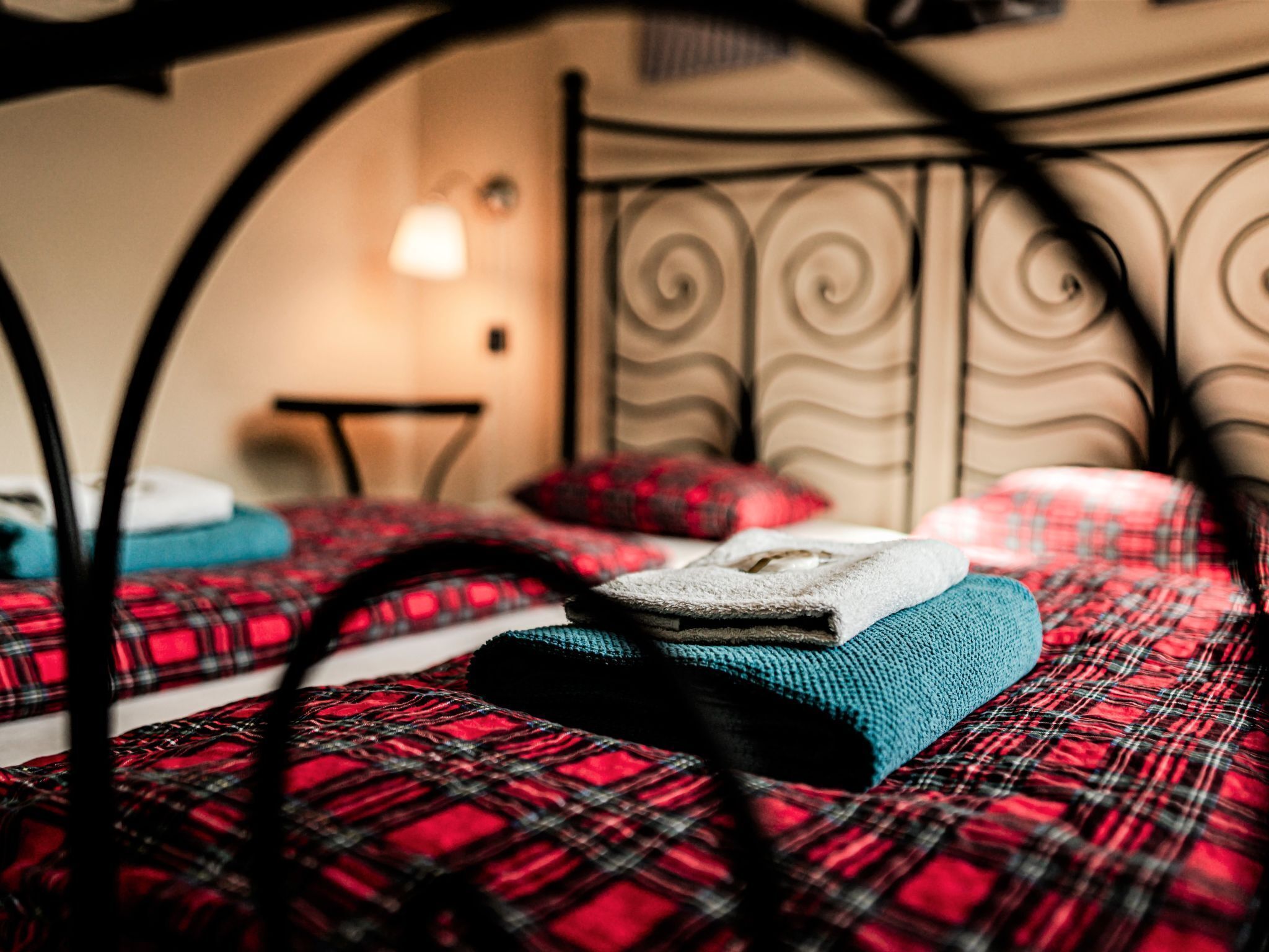 Una cama con una colcha escocesa roja, una manta verde azulada y una toalla blanca.