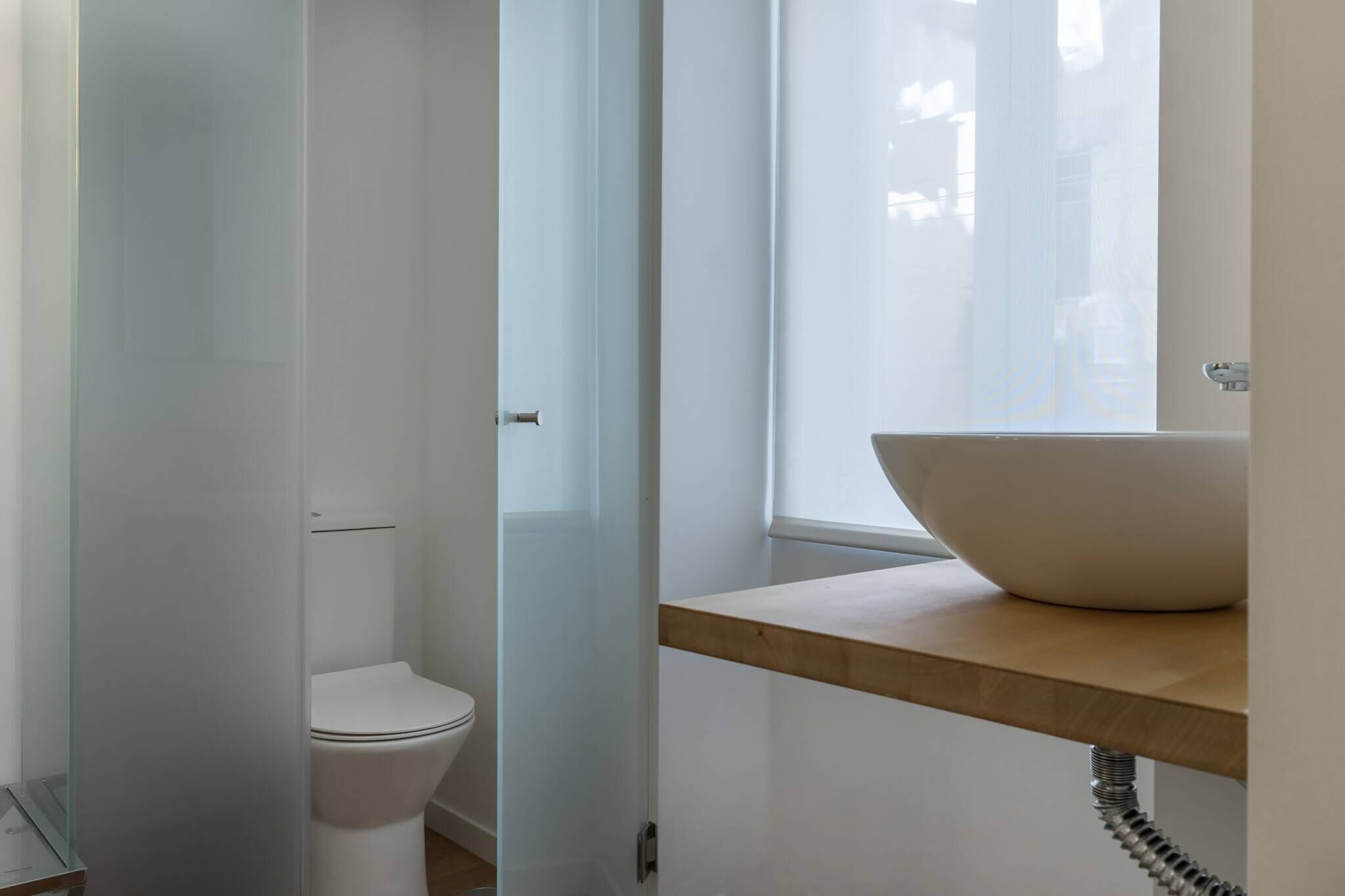Ein modernes Badezimmer mit Duschkabine aus Glas, einer weißen Toilette und einem hölzernen Waschtisch mit großem, weißem Becken.