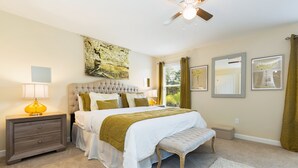 Ein Schlafzimmer mit einem großen Bett, einem Nachttisch, einer Bank, einem Deckenventilator und Kunstwerken an den Wänden.