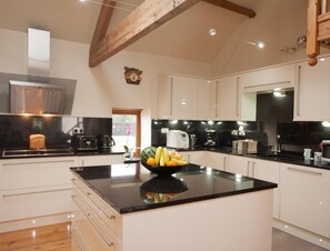 A modern kitchen with white cabinets, a black countertop, and a fruit bowl. - Beudy Bach (Llanelli)