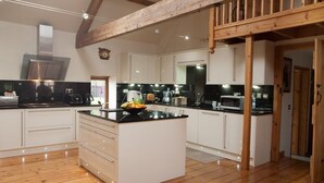 A spacious kitchen with wooden beams, white cabinets, and a central island with fruit. - Beudy Bach (Llanelli)