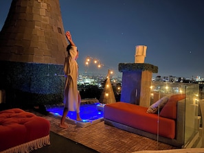 Terraço no terraço com banheira de hidromassagem, guarda-corpo de vidro e vista noturna da cidade.