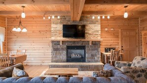 A cozy log cabin interior with a stone fireplace, a television mounted above it, and a comfortable seating area with a sofa and chairs. - Cozy Lodge Fireplace Suite in Ohio's Amish Country (Millersburg)