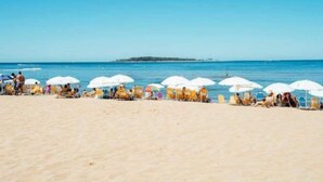 Ein Strand mit Liegestühlen und Sonnenschirmen unter blauem Himmel.