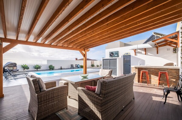 A covered outdoor area with wicker furniture, a pool, and a bar area.